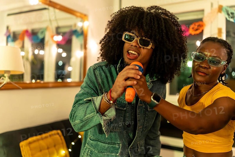 Latin man singing karaoke helped by woman at night party at home
