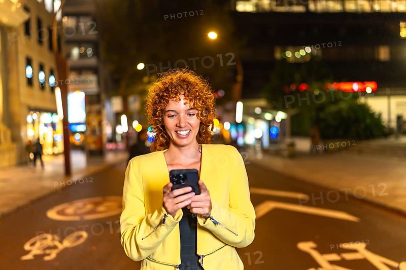 Frontal view of a happy casual woman using phone walking along the city at night