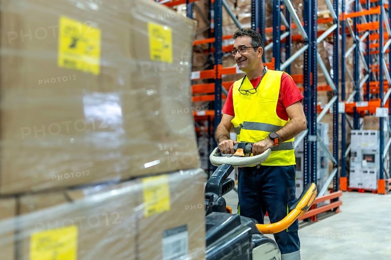 Mature happy man working in a warehouse moving boxes with forklift