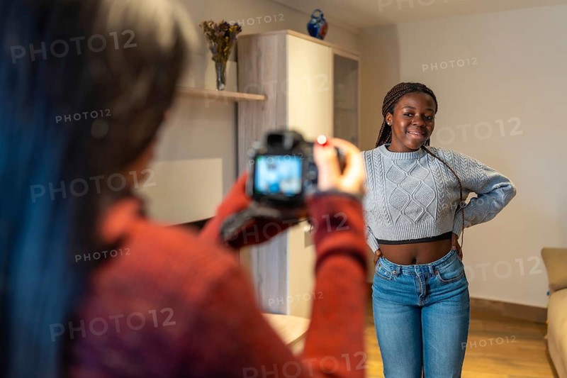Photographer capturing her beautiful friend posing joyfully in the cozy living room, celebrating friendship and creativity in a relaxed atmosphere