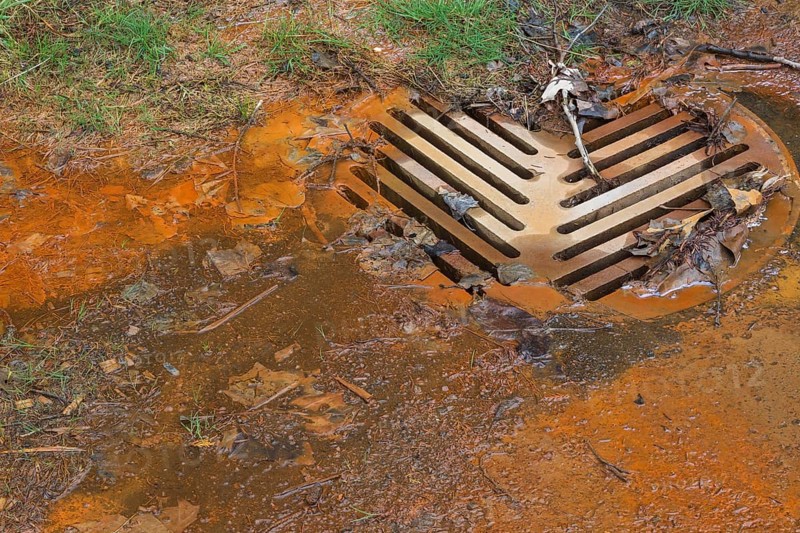 Contaminated rust colored water draining into sewer system at edge of a grass lawn in spring, Quebec, Canada, North America