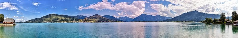 Clear water of a lake with surrounding mountains, on a sunny day with blue sky and white clouds, Tegernsee, Panorama