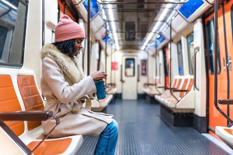 Passenger opening a reusable coffee cup while enjoying a quiet moment on a nearly empty subway train during the winter commute