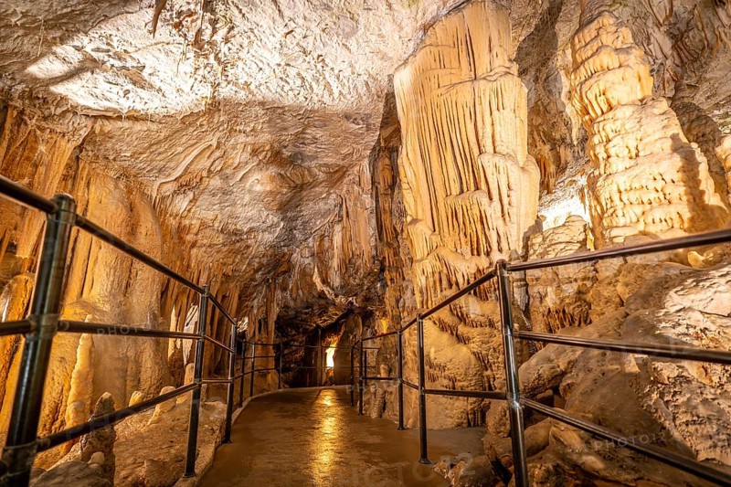 Tourists walking on illuminated pathway, admiring stalactites and stalagmites inside postojna cave, a famous natural attraction in slovenia