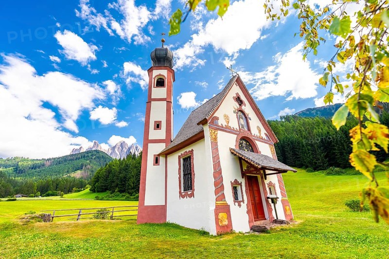 Charming st. Magdalena church nestled in a green meadow, with the majestic odle mountains and lush forests creating a stunning backdrop