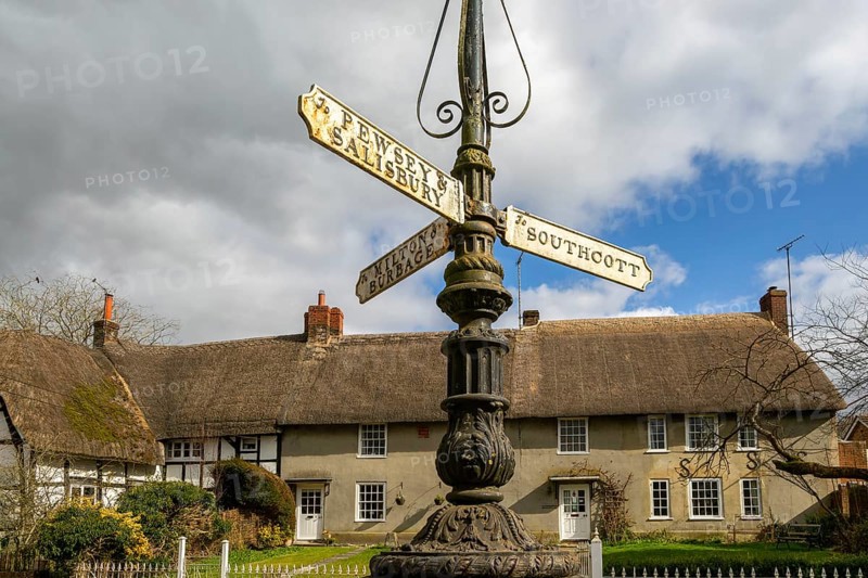 Historic signpost with direction painters, thatched cottages in village of Pewsey, Wiltshire, England, UK