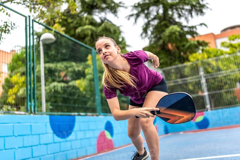 Energetic and sportive blonde young woman playing pickelball in an outdoor court