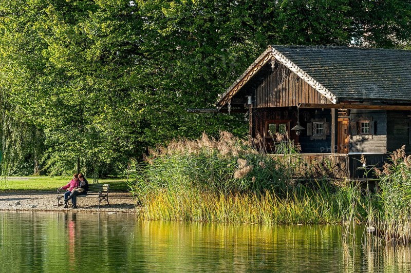 Wooden hut with common reed (Phragmites australis), two woman on a park bench, shore of Lake Schliersee, spa garden Markt Schliersee, Upper Bavaria, Bavaria, Germany, Europe