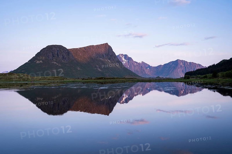 Landscape on the Lofoten Islands. Vagspollen bay, with Offersoykammen mountain behind it. The mountain Stornappstinden on Flakstadoya in the background. The mountains are reflected in the water. At night at the time of the midnight sun in good weather. Early summer. Vestvagoya, Lofoten, Norway, Europe