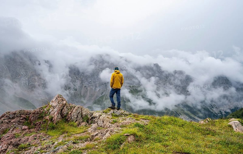 Mountaineer with yellow jacket looking at mountain landscape, cloudy rocky mountain peaks Wolayer Köpf and Biegenköpfe, Carnic Alps, Carnic High Trail, Carinthia, Austria, Europe