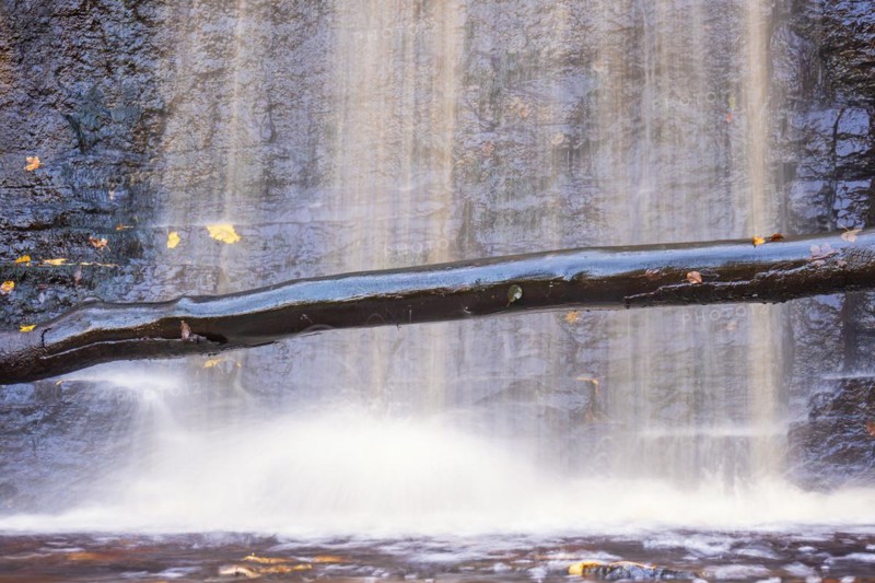 Tree log by a waterfall with falling water by a rock face