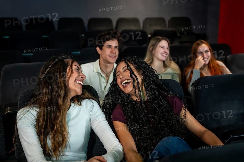 Friends enjoying laughter together while watching a comedy film at the cinema, sharing moments of joy and fun in a vibrant atmosphere