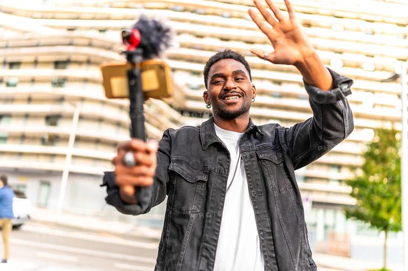 African man vlogger waving at camera while recording video blog in the city