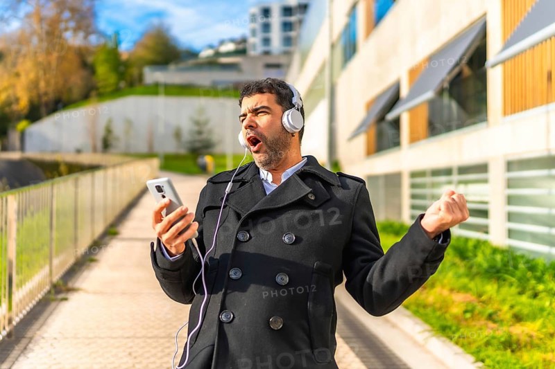 Happy adult man in elegant clothes enjoying listening to music, singing and dancing at city in winter