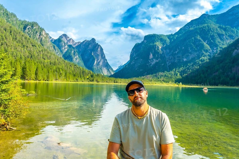 Tourist relaxing by lake dobbiaco, surrounded by the stunning peaks of the dolomites on a beautiful summer day in italy