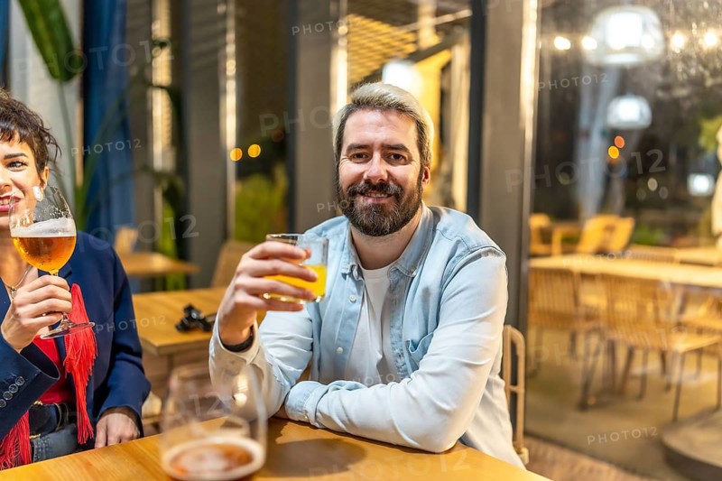 Man drinking cocktail with friends enjoying night life sitting relaxed on a roof terrace of a bar