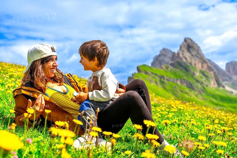 Tourists relaxing in a dandelion field, enjoying the view of the seceda mountains in the italian dolomites during a sunny summer day