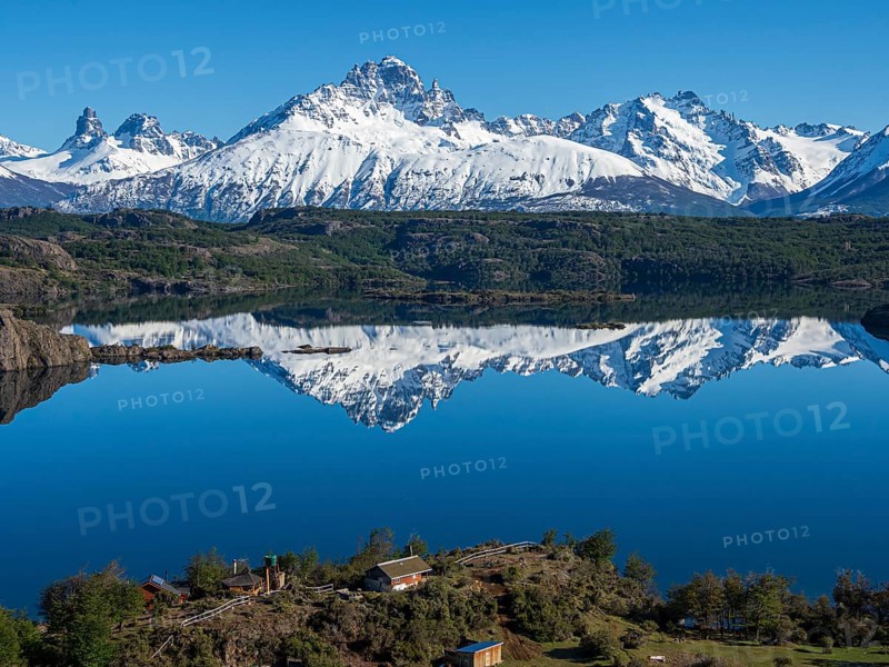 The snow-covered Mt. Cerro Castillo is reflected in a lake, small farm by the lake, Patagonia, Chile, South America