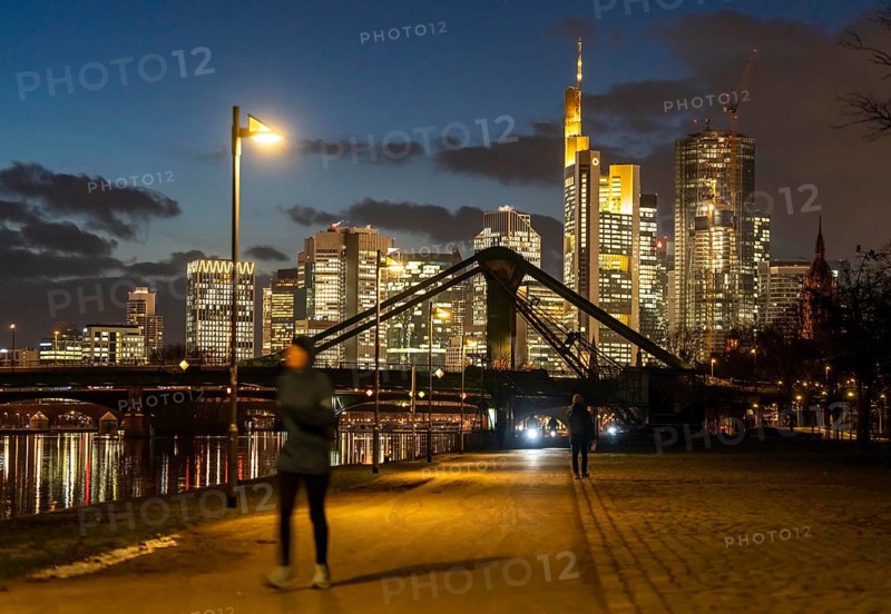 Skyline of the city centre of Frankfurt am Main, joggers on the pavement, promenade along the river Main, dusk, Hesse, Germany raft bridge in the background