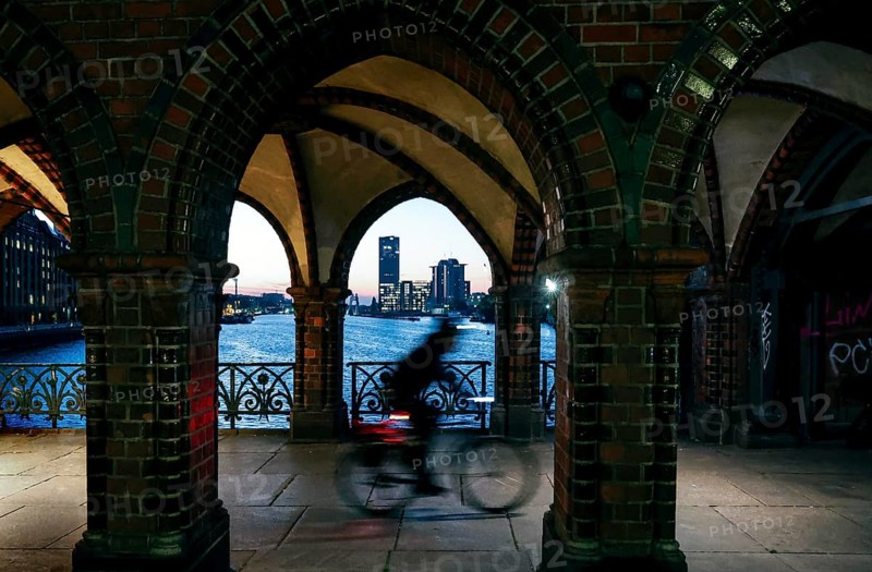 Bicycle rider to the sunrise at the Oberbaum Bridge, view through the arcades over the Spree to the Treptower Towers, Berlin, 17.10.2024, Berlin, Berlin, Germany, Europe