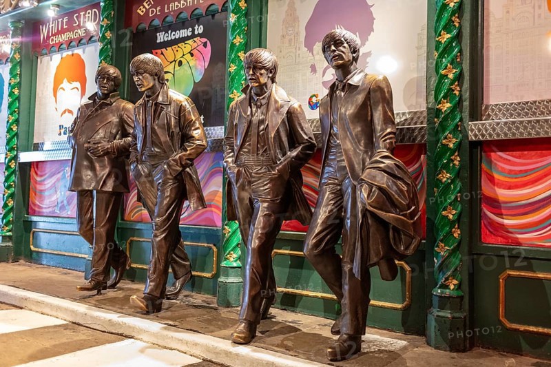 Four bronze statues depict people in motion in front of a decorated block, Liverpool