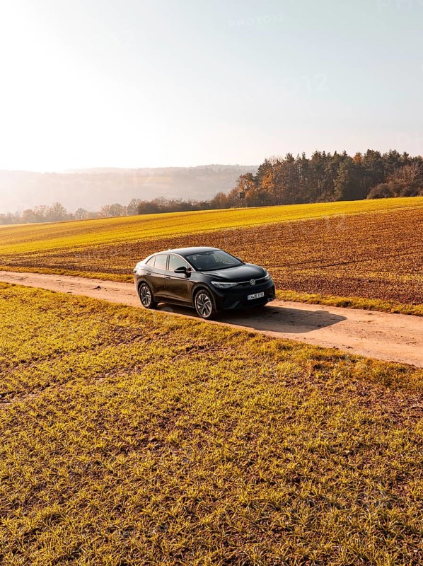 A car drives alone on a country lane, surrounded by golden fields under the sun, electric car VW ID5, Deer Carsharing, Gechingen, Black Forest, Germany, Europe
