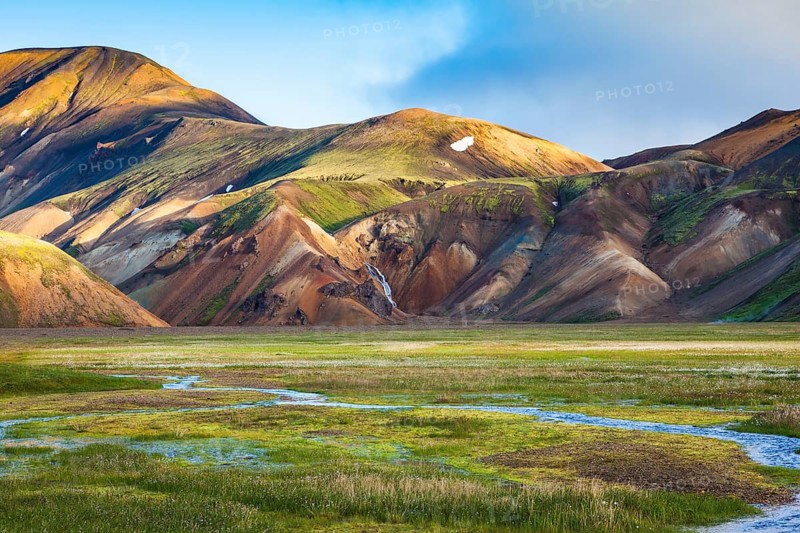Green Valley is flooded with melt water. Snow lies in the hollows of colorful rhyolite mountains. Early summer morning in the National Park Landmannalaugar, Iceland, Europe