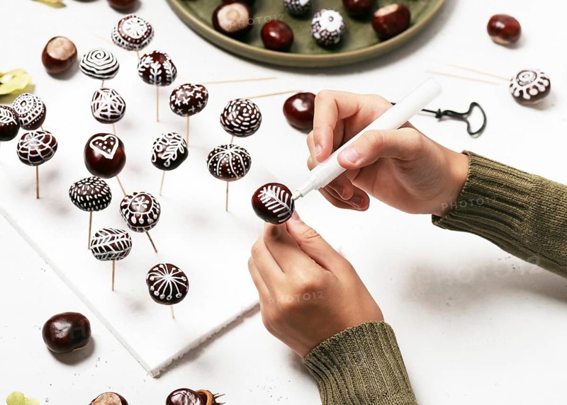 Chestnuts painted with white acrylic pen. Creative autumn decoration with natural material. Handicrafts, handicrafts with children