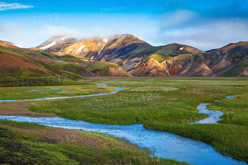 Snow lies in the hollows of colorful rhyolite mountains. Green Valley is flooded with melt water. Early summer morning in the National Park Landmannalaugar, Iceland, Europe