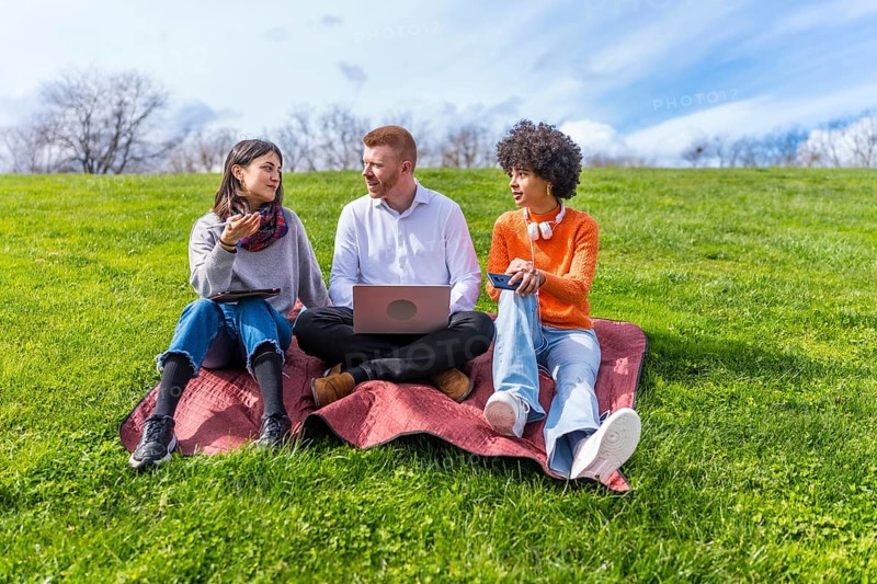 Three young entrepreneurs working outdoors, using technological devices, enjoying a sunny spring day