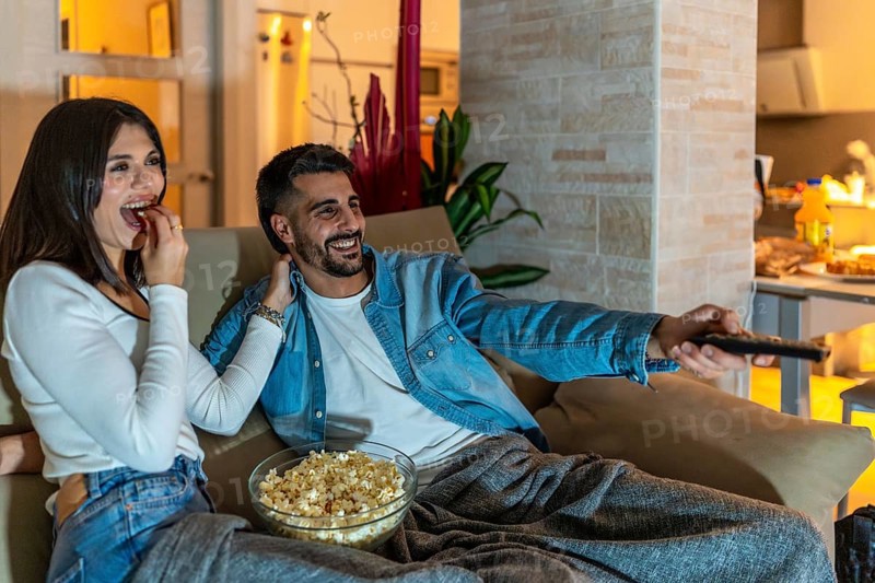 Young couple relaxing on a cozy sofa, enjoying a movie night filled with laughter, popcorn, and the warmth of togetherness