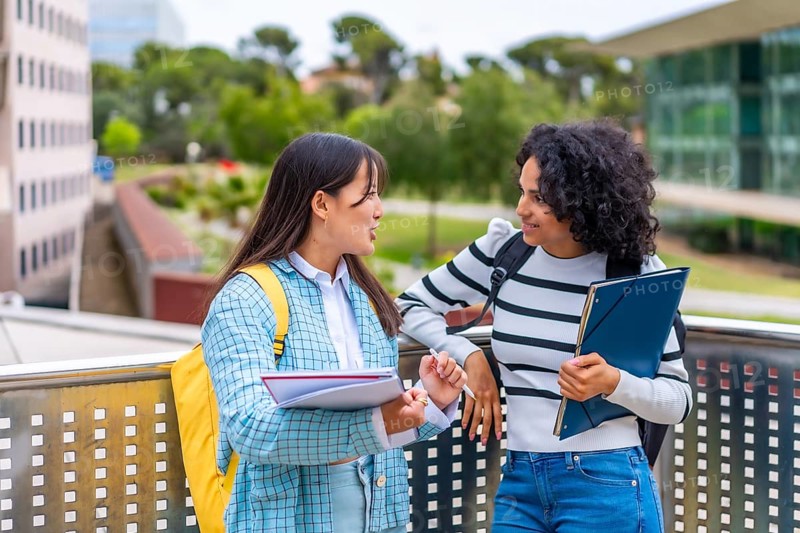 Two multi-ethnic female students reading and commenting notes standing outside the campus