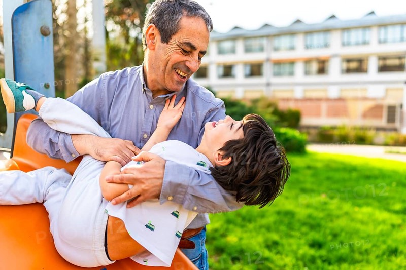 Grandfather holding and playing with his grandson at the playground, they are laughing and having fun together