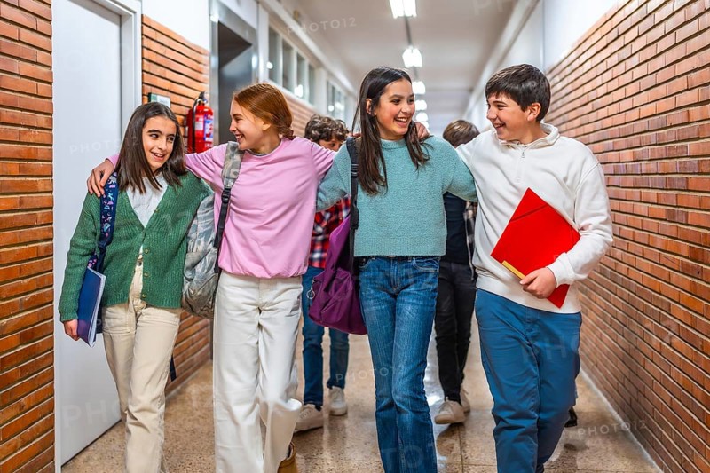 Group of cheerful students walking together in school hallway, enjoying their time together between classes