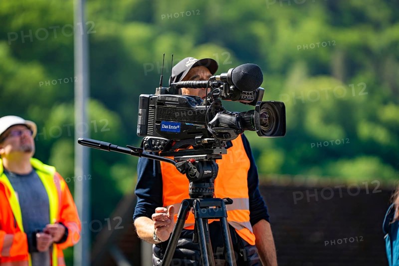 A cameraman in a brightly coloured waistcoat with a camera films outside in sunny weather against a green background, Hermann Hesse Bahn bridge lift, Calw, Germany, Europe