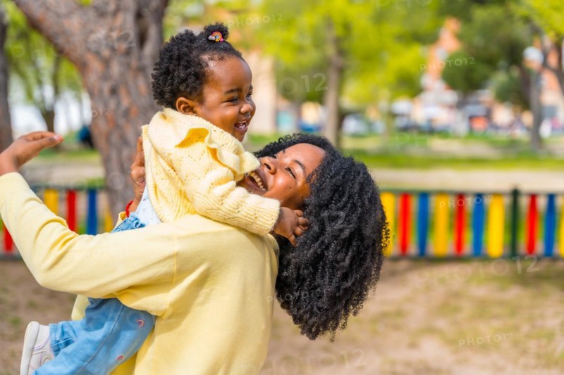 Joyful mother and adorable african girl embracing playing on a park