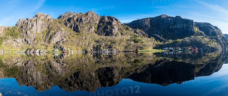 Near Ana-Sira at the norwegian southern coast, lonely houses at the foot of a rock formation are reflected in the calm sea, panorama, Norway, Europe