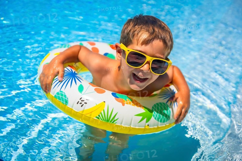 Boy having fun in the swimming pool with a floating rubber ring in summer