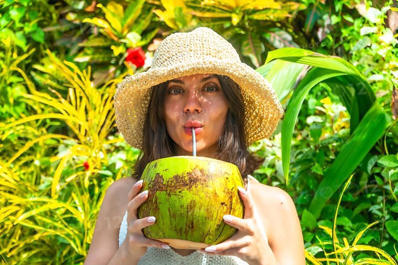 Young woman with straw hat savoring refreshing coconut water, surrounded by vibrant tropical foliage in siargao island, philippines