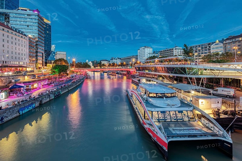 River scene with boats and illuminated city façade under a blue evening sky, Vienna