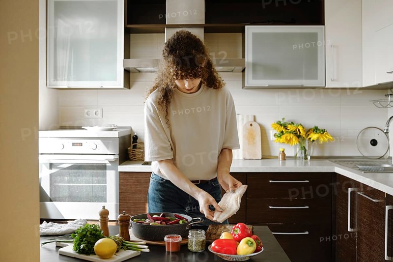 A woman is about to put fresh hake fillet on vegetables and bake the dish in the oven
