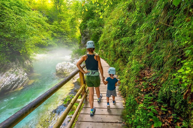 Mother and son wearing helmets are walking on a wooden pathway alongside a pristine river, enjoying the stunning scenery of vintgar gorge near bled, slovenia