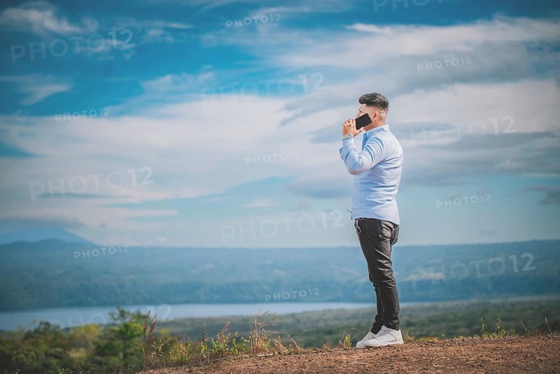Handsome young man talking on the phone outdoors surrounded by nature. A person talking on the phone in a beautiful scenic viewpoint