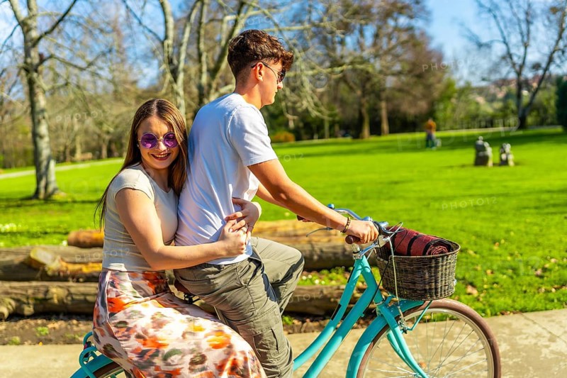 Romantic couple riding a bicycle together on a sunny day, enjoying the lush greenery of a vibrant park filled with joy and laughter