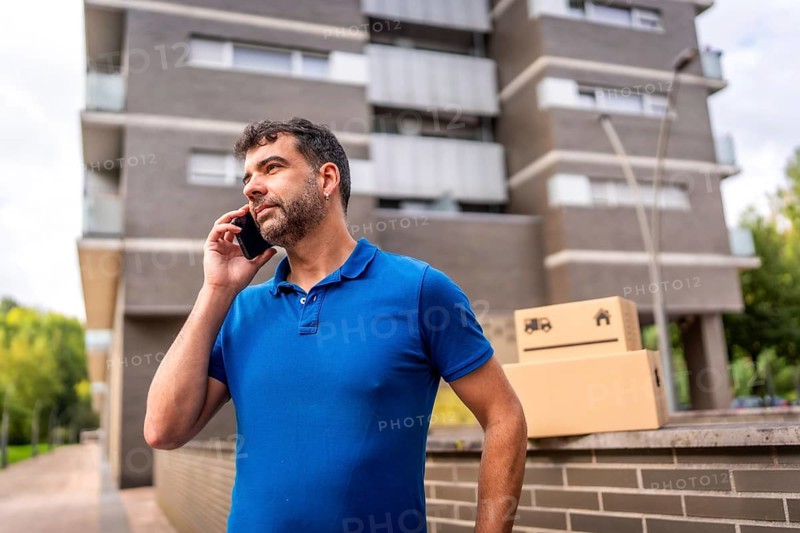 Delivery man talking to the mobile next to parcels to deliver outdoors