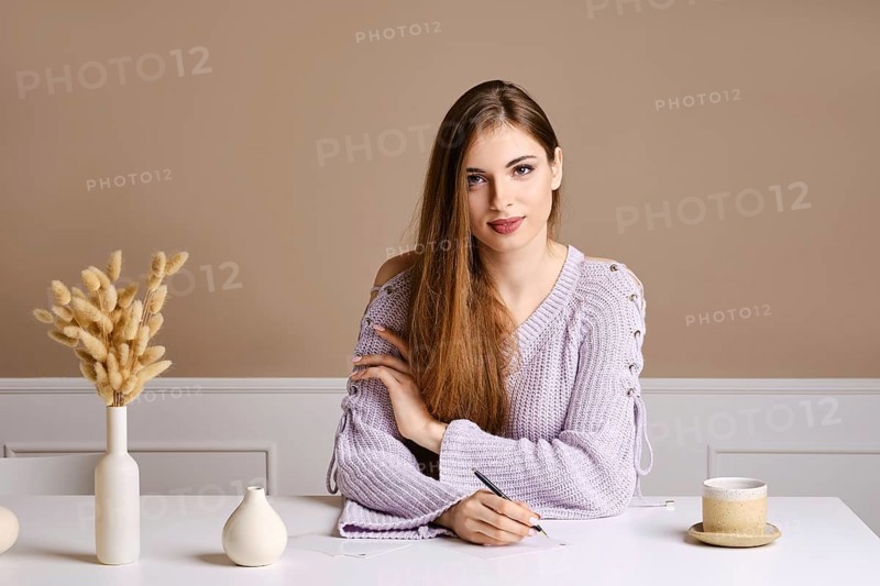 Kind young woman sits behind the table and signs greeting postcard