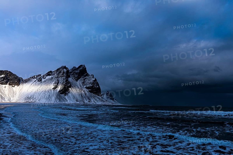 White foamy waves on the beach of Stokkness, behind snowy rocky slopes of Vestrahorn, near Höfn, Sudausturland, Iceland, Europe
