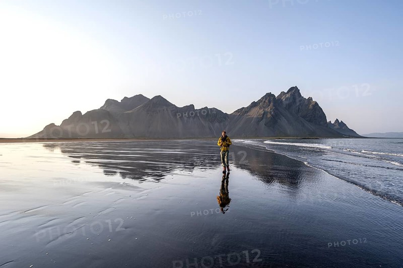 Tourist at black lava beach, sandy beach and sea, mountains Klifatindur reflected in the water, Eystrahorn and Kambhorn, headland Stokksnes, mountain range Klifatindur, Austurland, East Iceland, Iceland, Europe