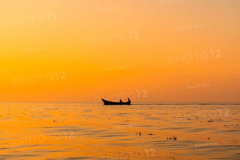 Fishing boat with a fisherman fishing in the orange sunset of Shkoder Lake in Shiroka. Albania