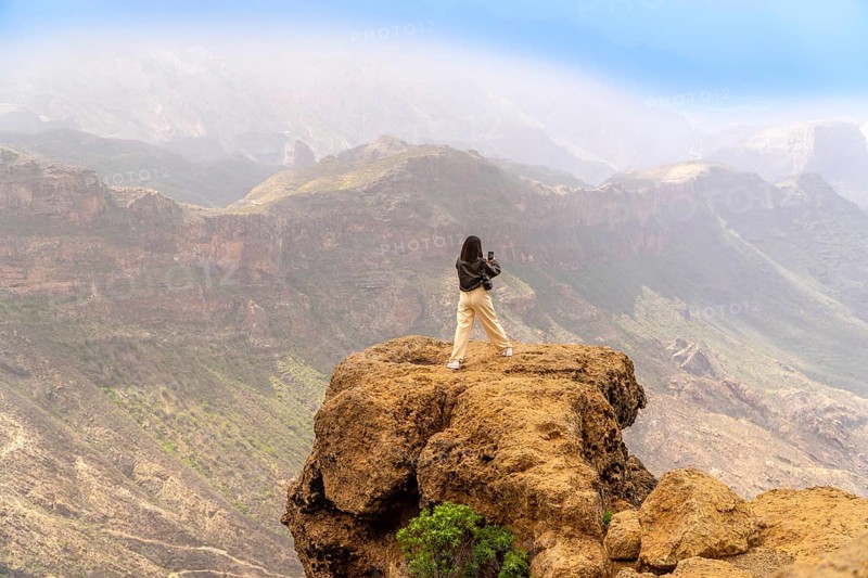 Woman photographing a scenic mountain range in gran canaria, canary islands, enjoying freedom and adventure in summer nature